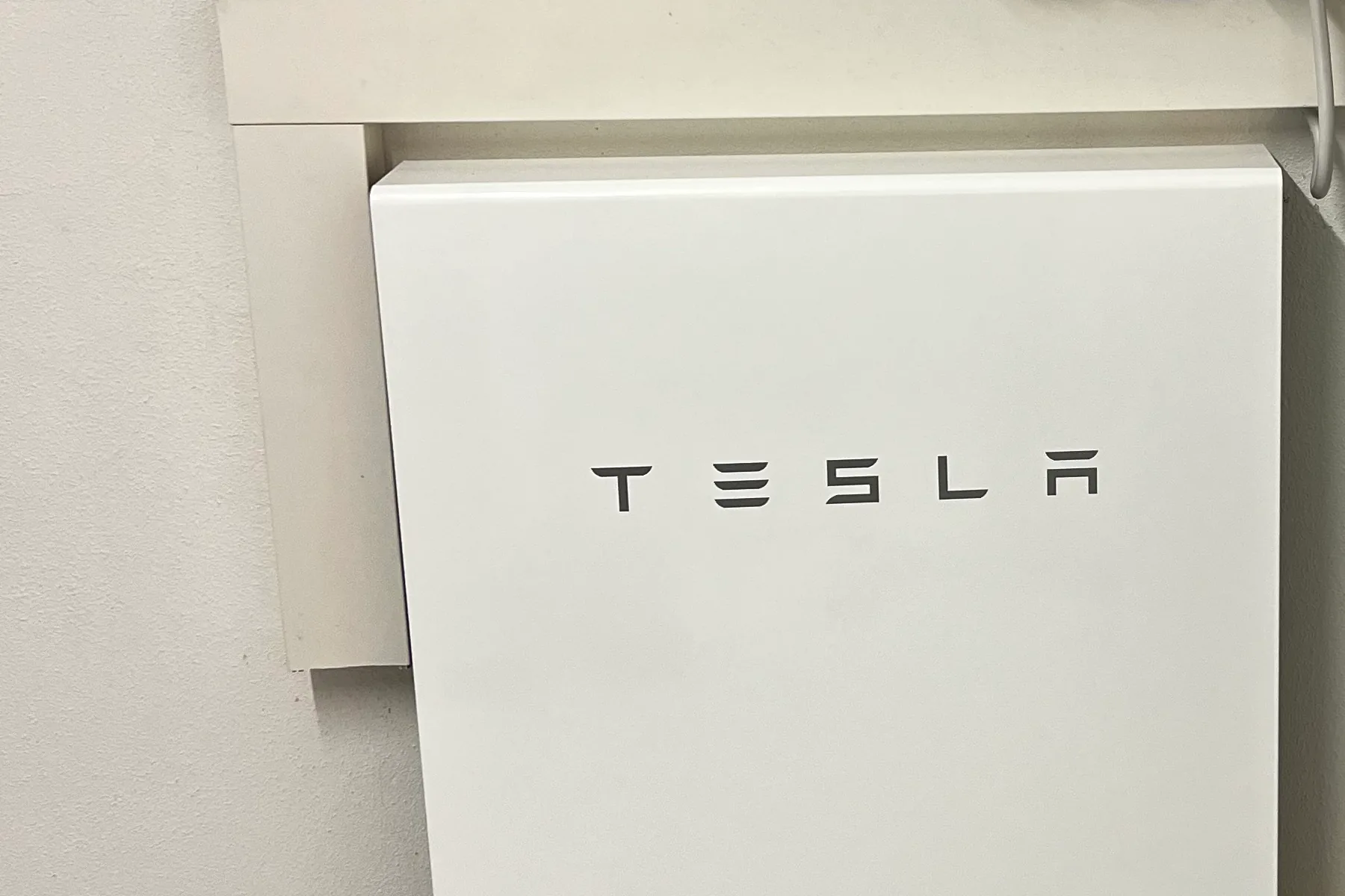 Weißer Batteriespeicher mit Tesla-Schriftzug an der Wand im Technikraum